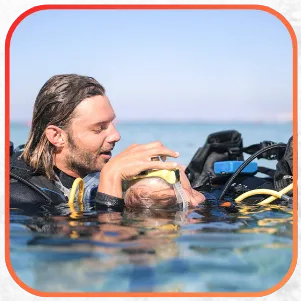 A diver assisting another diver at the surface of the water.