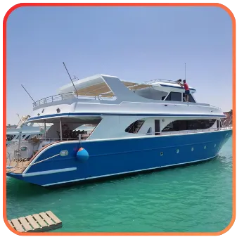 A luxury blue yacht with two decks and a sunbathing area, moored in a harbor with clear turquoise waters.