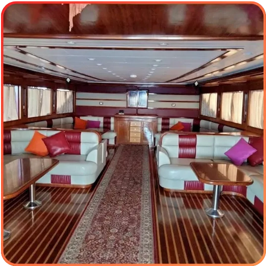 The interior of a boat's saloon with cream and burgundy sofas, wooden floors and walls, accentuated with decorative cushions and tables.