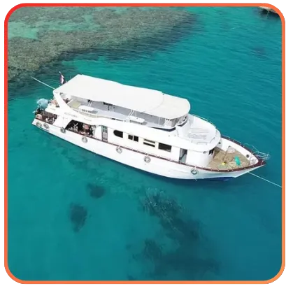 A luxury blue yacht with two decks and a sunbathing area, moored in a harbor with clear turquoise waters.