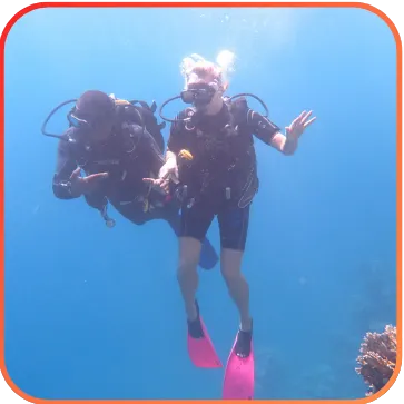 A diver in clear blue water gesturing 'OK' with a coral reef in the background.