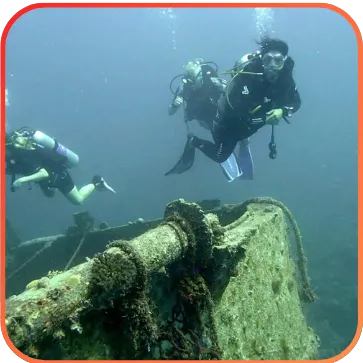 Divers exploring near an underwater structure covered in marine life.