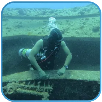 A diver exploring the edge of a sunken ship's structure, giving a sense of scale and the thrill of underwater discovery.