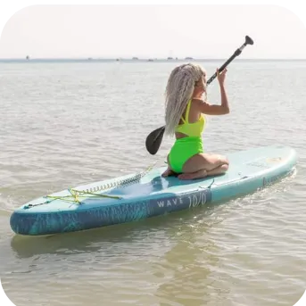 A woman with silver hair paddleboarding on calm water, wearing a bright yellow swimsuit, and holding a black paddle.