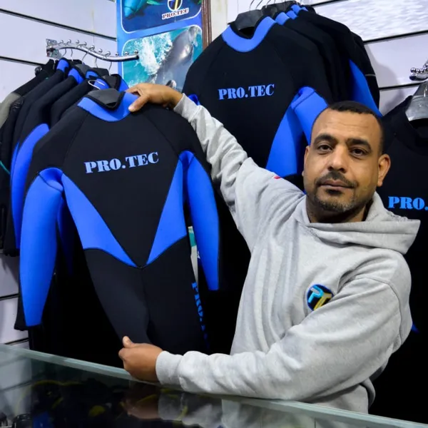 A person displaying a blue and black wetsuit in a dive shop.